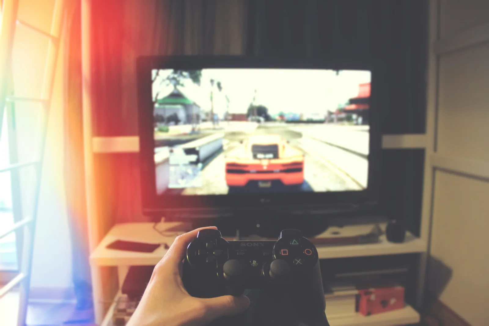 Eine Person hält einen PS3-Controller vor einem Flachbildschirm, auf dem GTA 5 läuft.